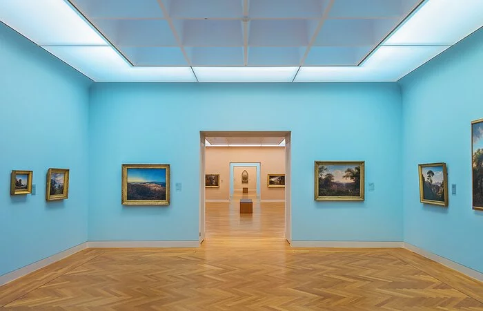 Ausstellungsraum mit hellem Holzboden und blauen Wänden mit Gemälden