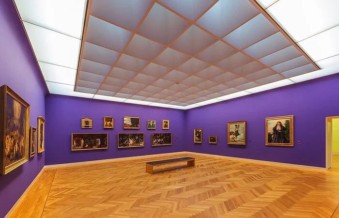 Ausstellungsraum mit hellem Holzboden und lila Wänden mit Gemälden