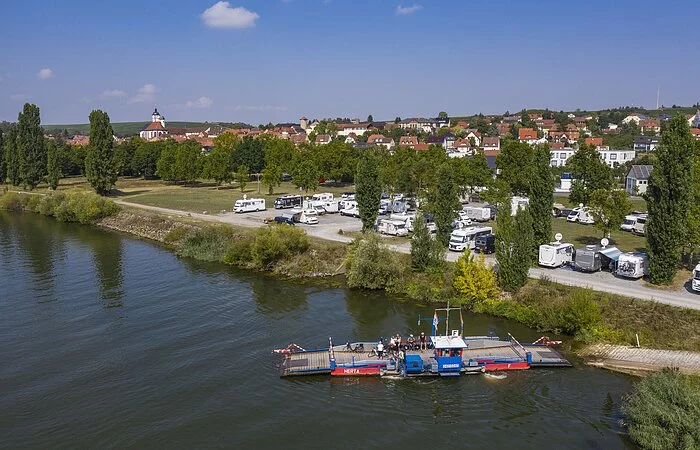 Main und Weg parallel dazu mit Wohnmobilen, Bäumen und Blick zur Ortschaft