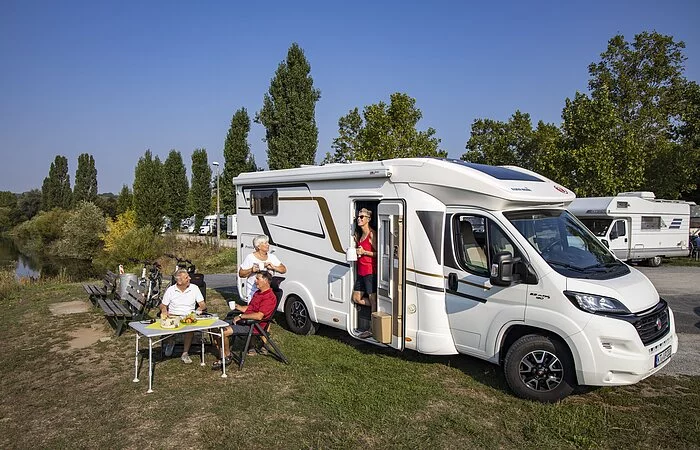 Personen am Tisch beim Essen vor einem Wohnmobil direkt am Main