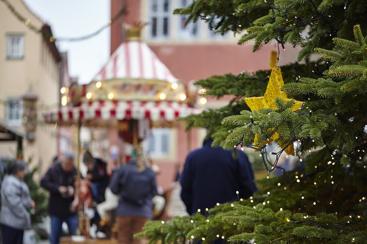 Ein goldener Weihnachtsstern hängt an dem Weihnachtsbaum. Im Hintergrund Personen