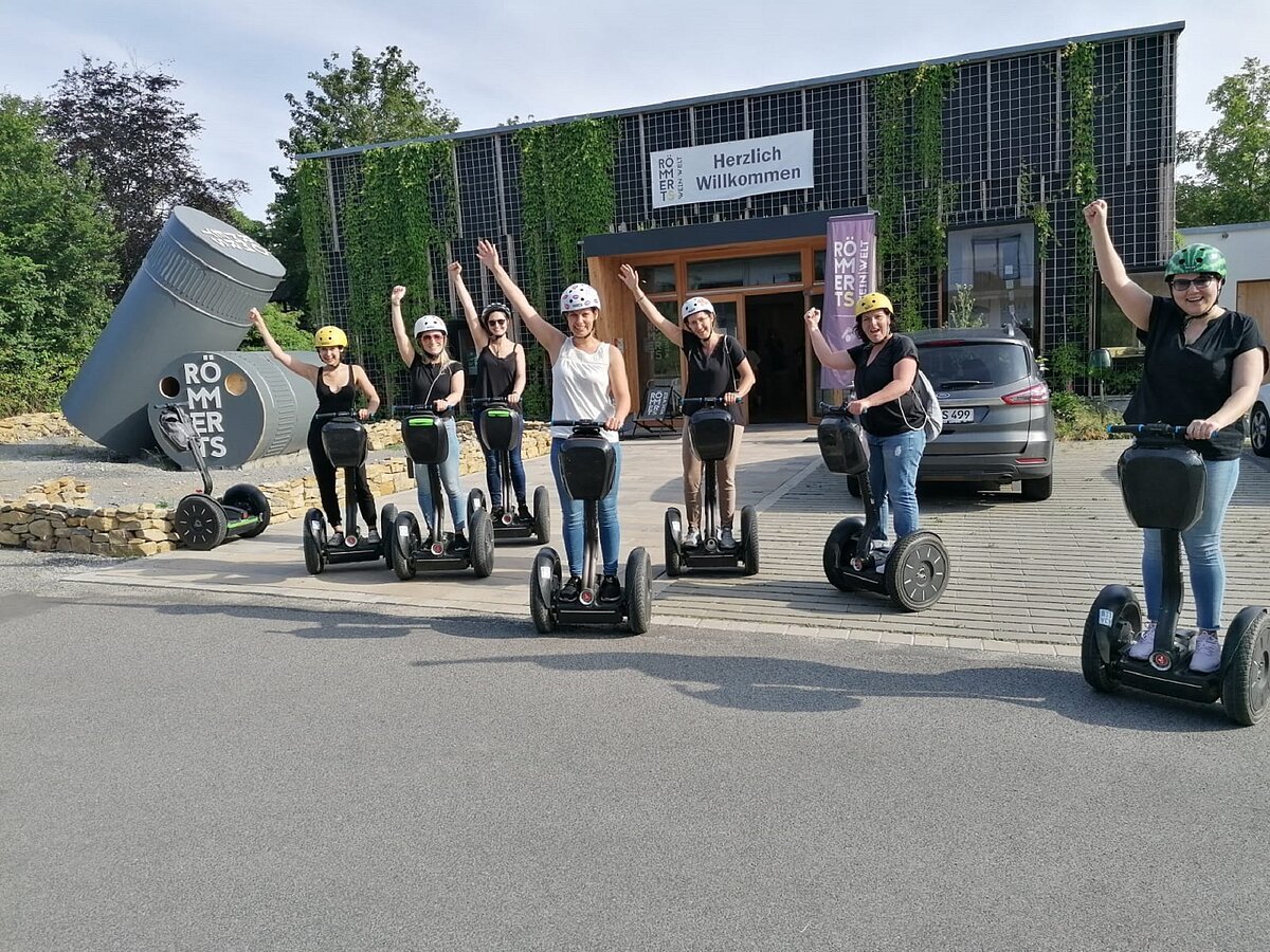 Gruppe im Freien auf Segways vor einer großen Halle