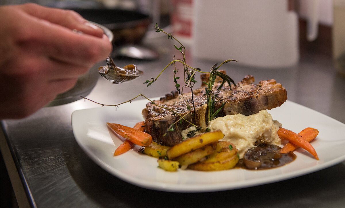 Ein Koch der Iphöfer Gastronomie richtet auf einem Teller ein Fleischgericht mit Gemüse, Kräutern und Soße an