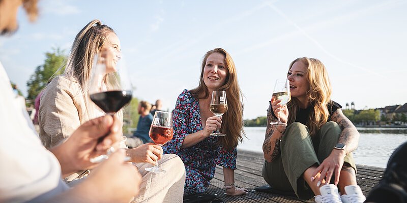 Eine Personengruppe sitzt am Kitzinger Main und trinkt ein Glas Wein.