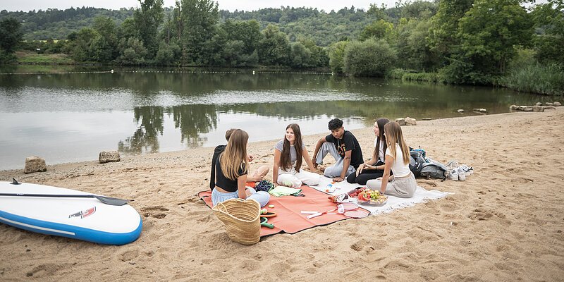Eine Gruppe an Jugendliche picknickt am Mainufer in Eibelstadt