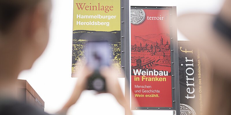 Eine Frau fotografiert mit ihrem Smartphone die drei Fahnen des Terroir f in Hammelburg