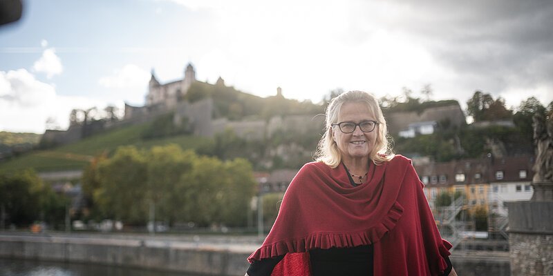 Maria Pertmann Ley, Leiterin Touristinformation Würzburg steht auf der Alten Mainbrücke in Würzuburg. Im Hintergrund die Festung Marienberg.