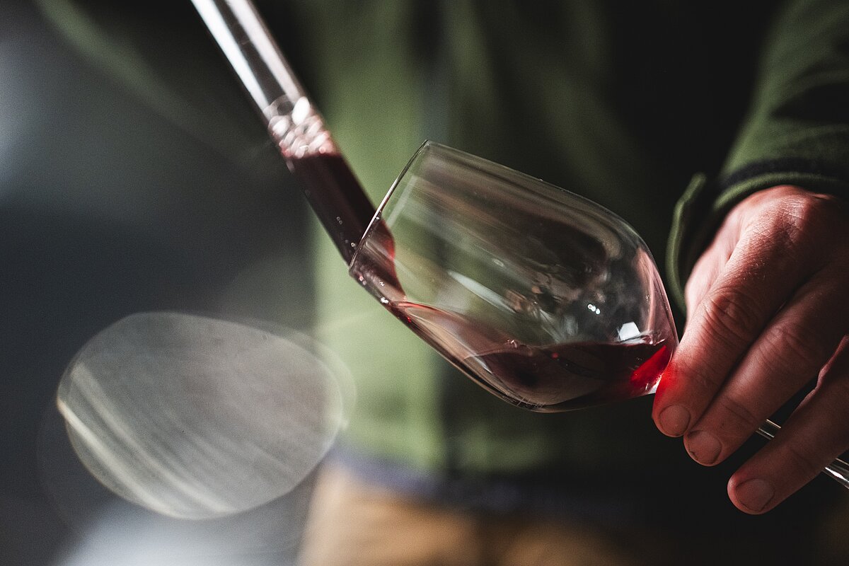 Mit einer Pipette wird Rotwein aus dem Holzfass geholt und in ein Weinglas gegeben