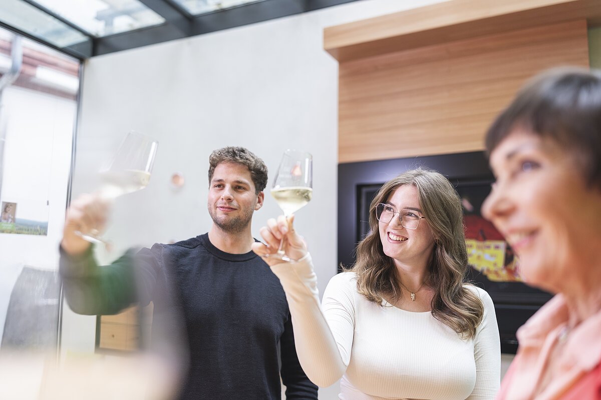 Drei Personen schauen lachend Weingläser bei einer Weinprobe an