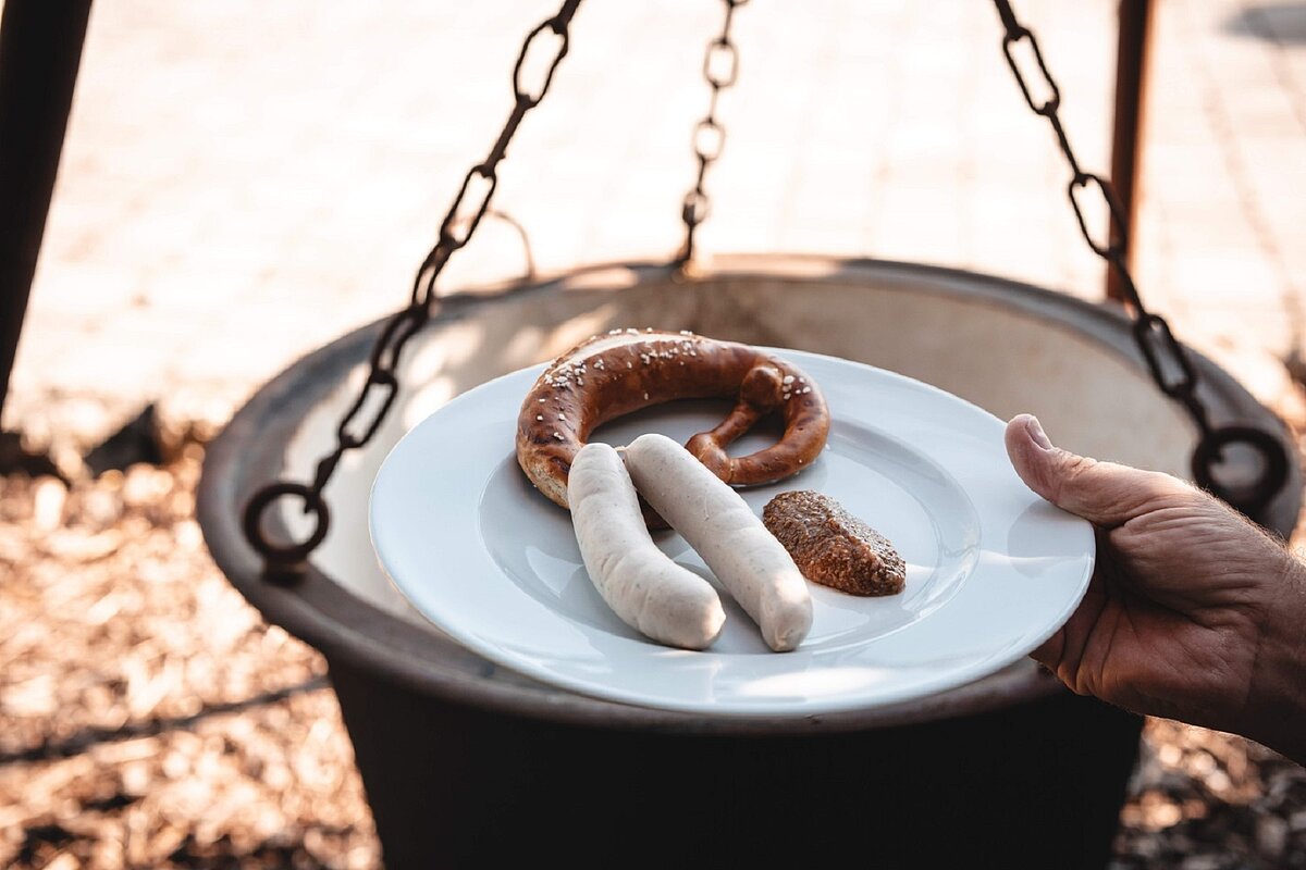 Wurstkessel über offenem Feuer sowie Teller für Weißwürste, Breze und Senf